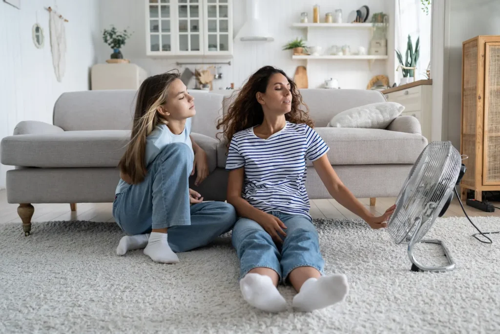 Mom and daughter sitting next to a fan on the floor of the living room.