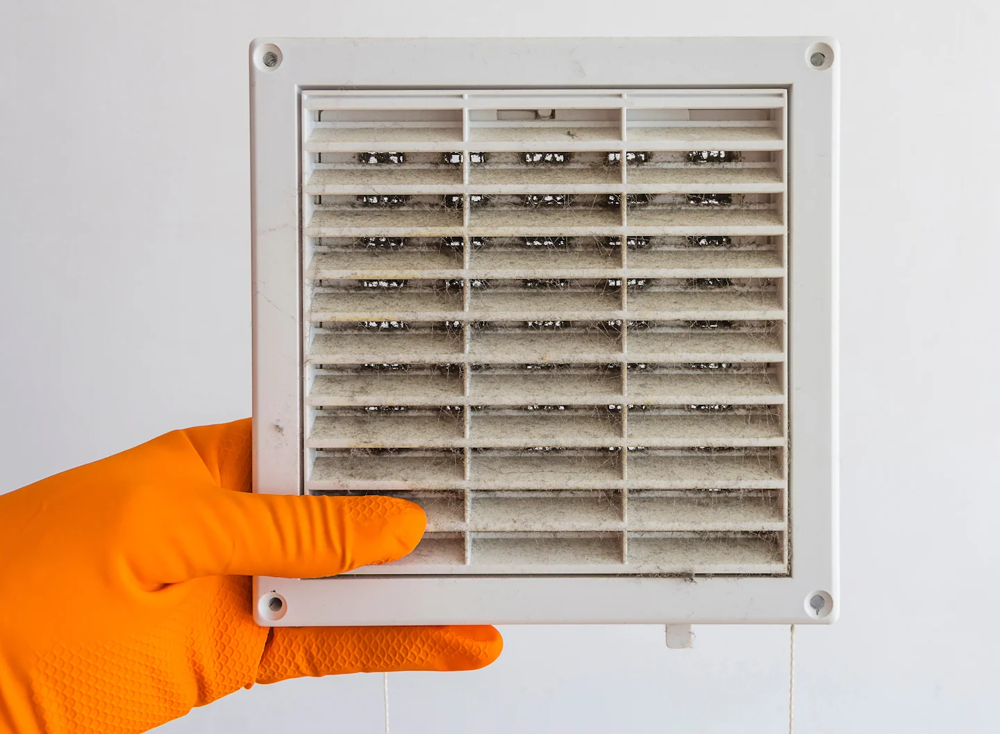 Hand inside orange glove holding dusty air vent plate cover. 