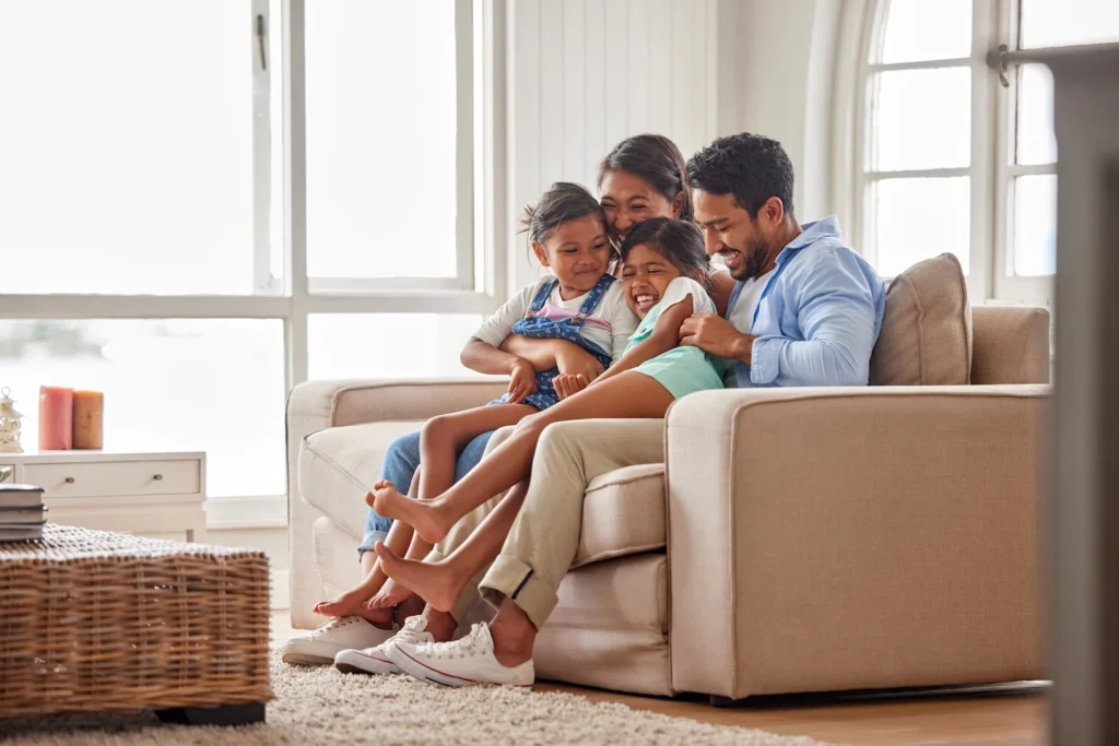 Family sitting on couch and laughing inside home with air conditioning.
