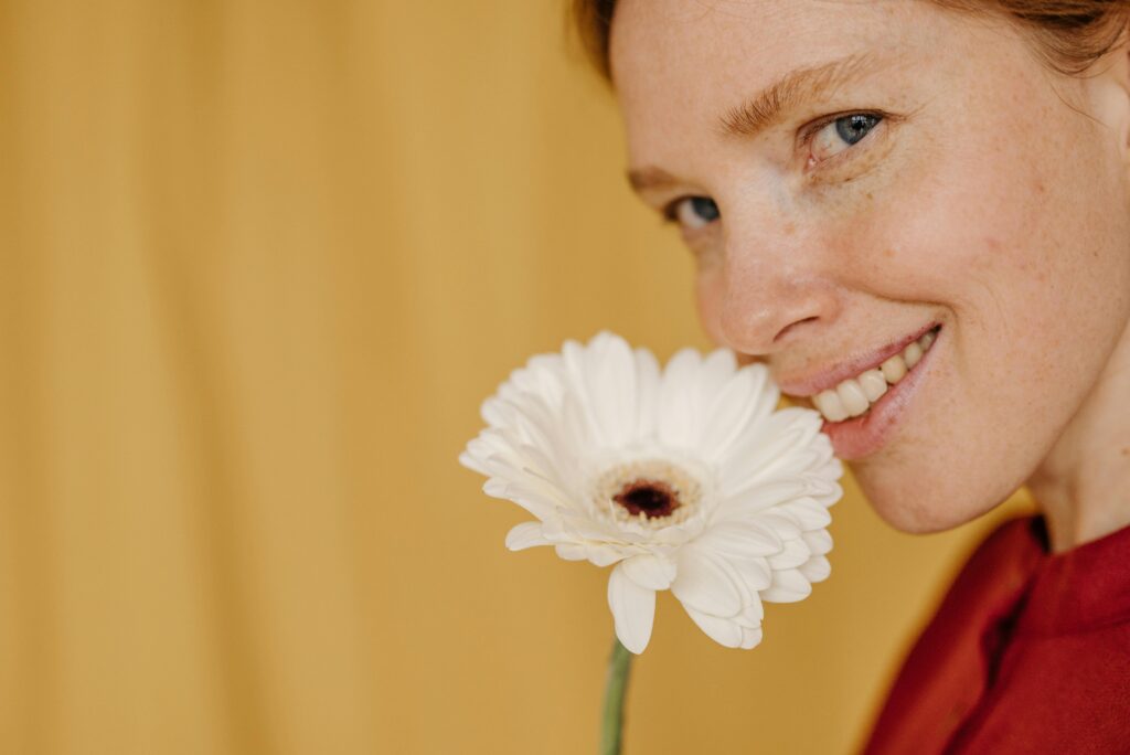 Smiling woman holding white gerbera daisy to her face.