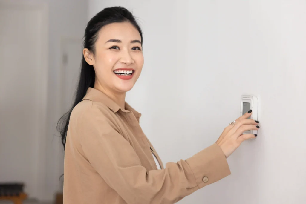 Woman smiling while adjusting a thermostat on the wall of her home